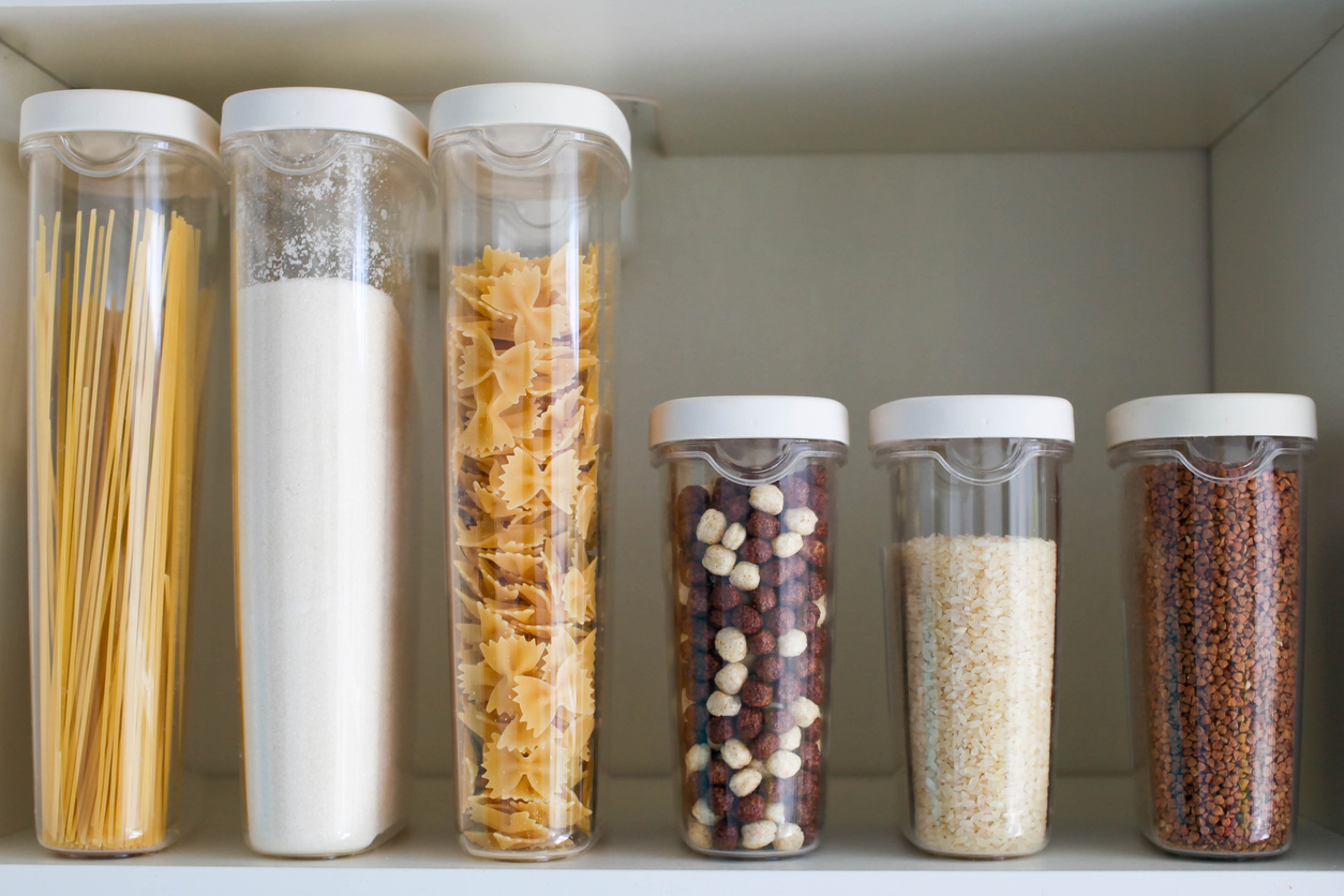 A pantry with pasta, sugar, nuts, and rice organized in plastic containers.