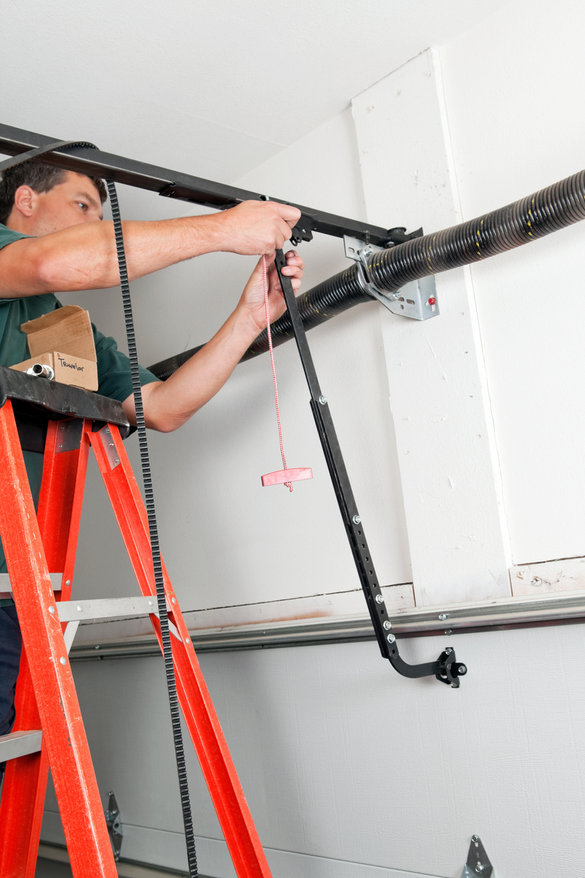 A worker is replacing the traveler car on a belt driven garage door opener.