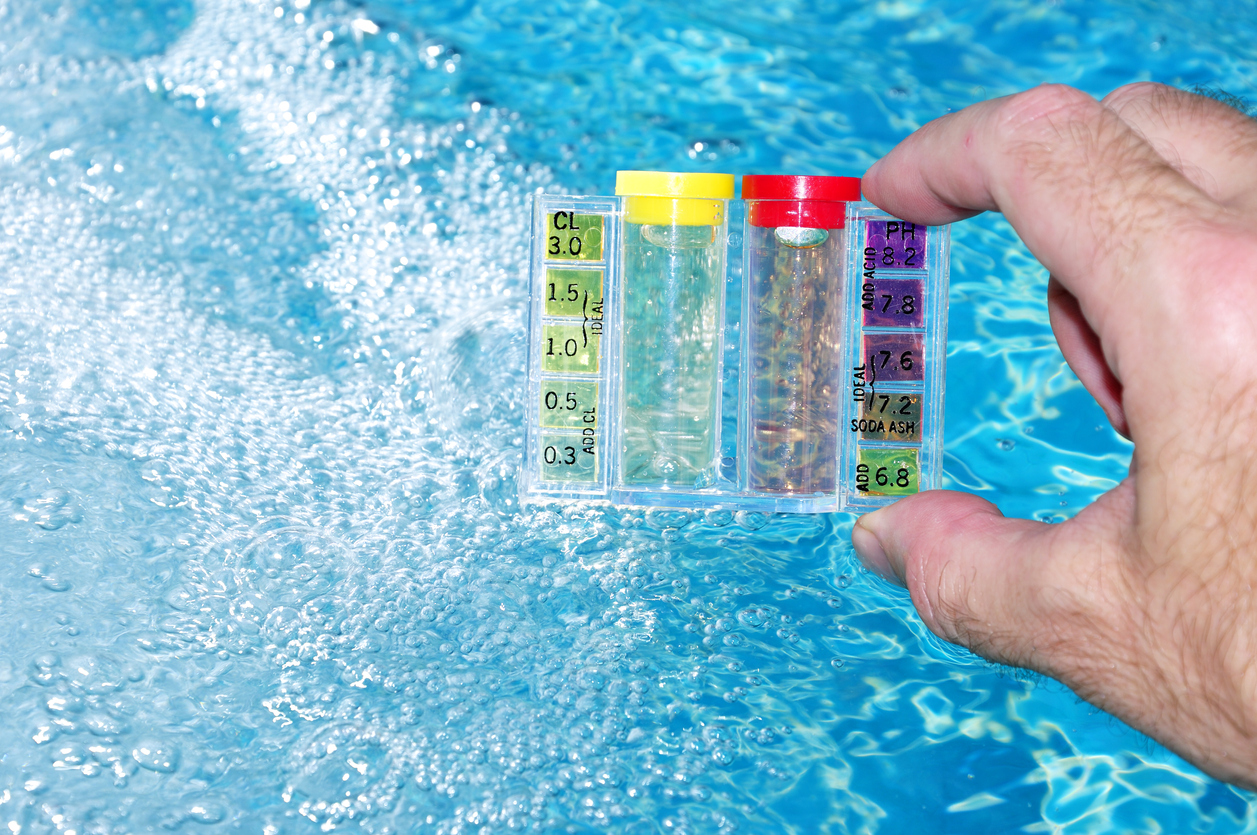 A hand holding a water test kit with pool water background.
