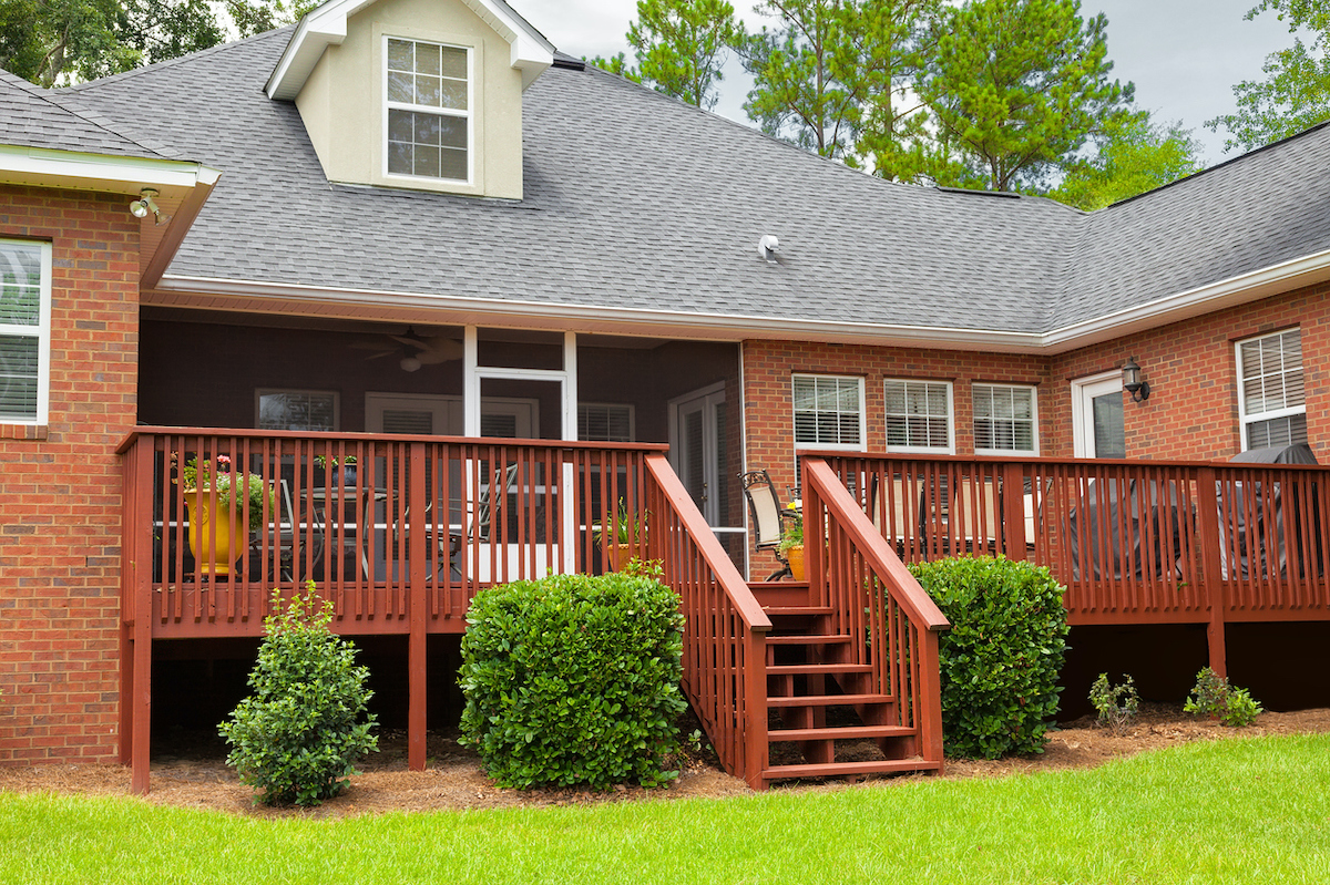Red brick house with red-stained deck and stair in backyard.