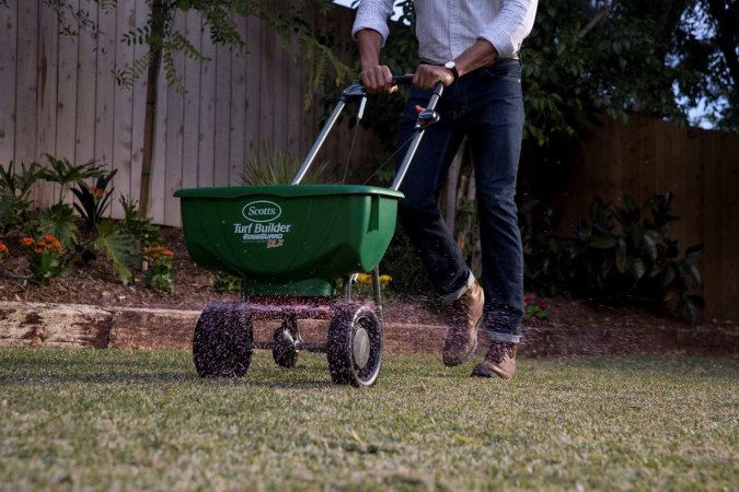 A man using a fertilizer spread to spread the best fertilizer for centipede grass option