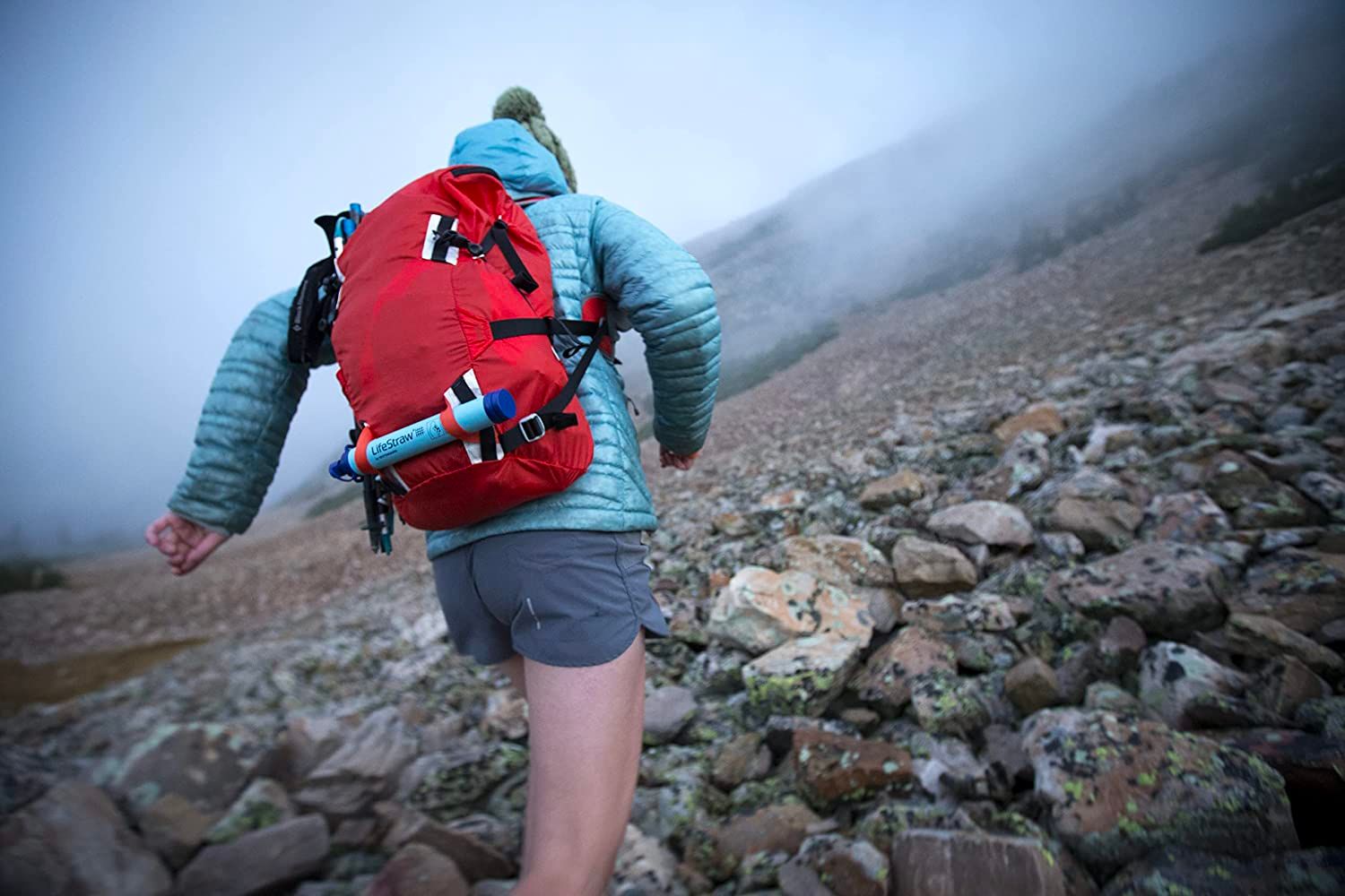 A hiker traverses rocky terrain with the best portable water filter option attached to their backpack