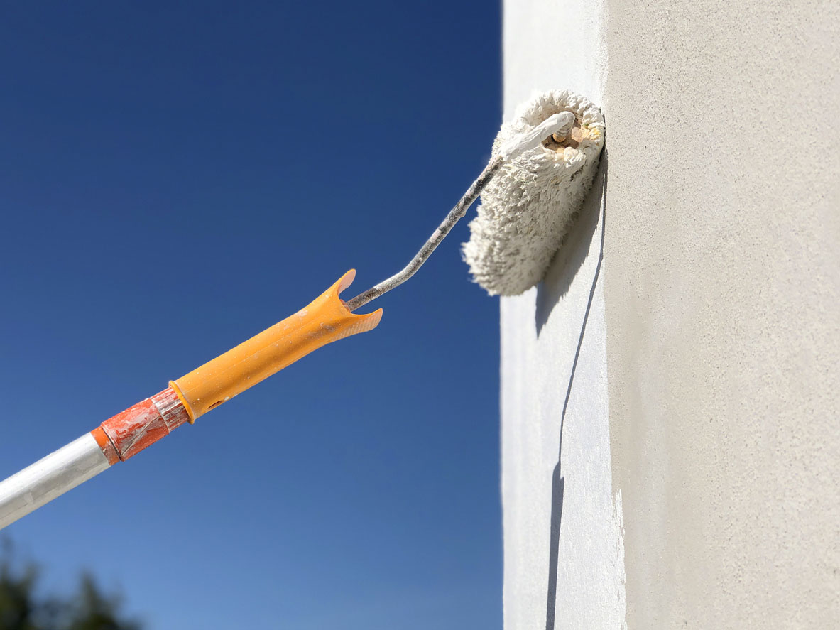 A close up of a paint roller that's being used to paint the exterior of a house.