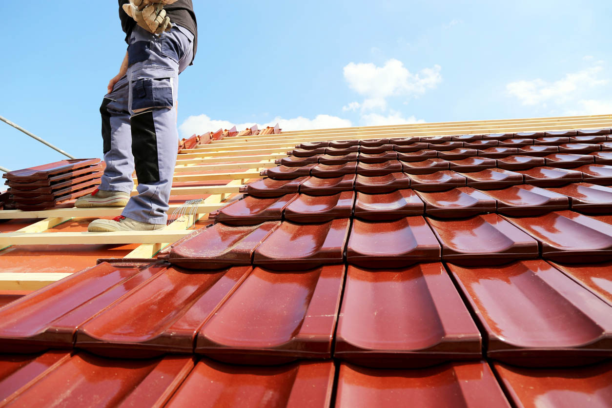 A roofer is in the process of installing a new red tile roof.
