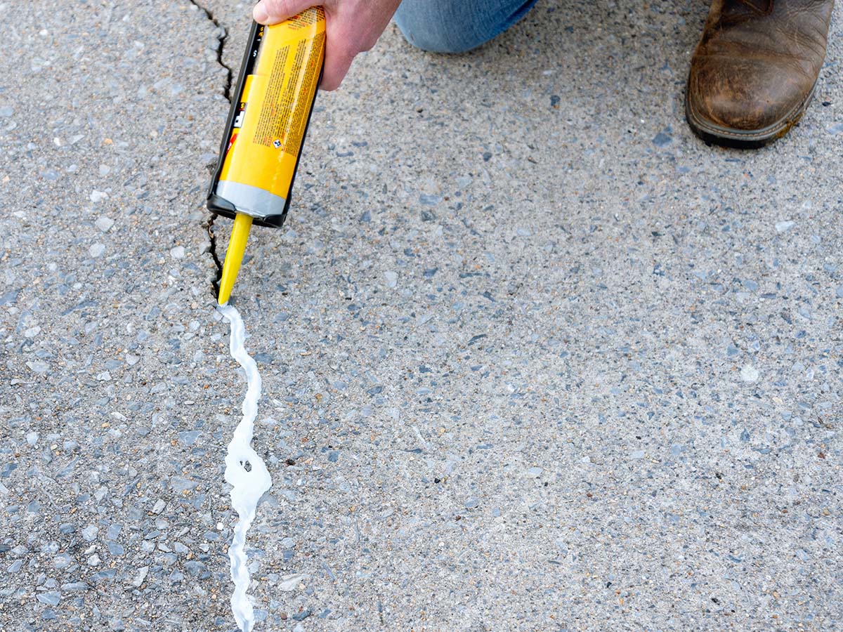 A person using the Sikaflex Self-Leveling Sealant to fill a large concrete crack.