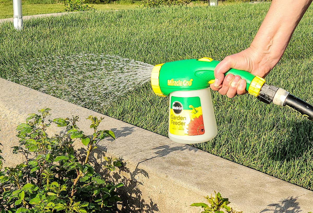 Person using Miracle-Gro hose end sprayer on plants near patio