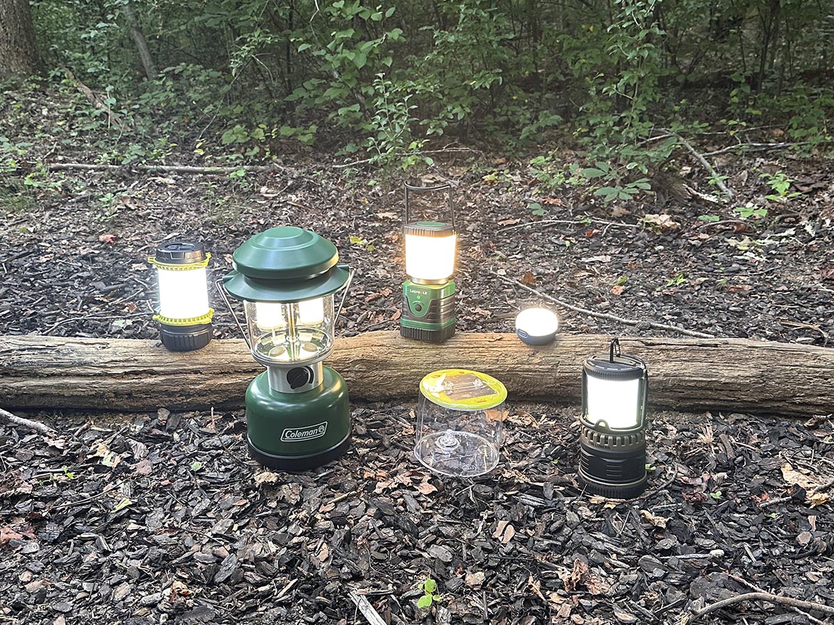 A group of the best LED lantern options lit up on the ground in a wooded area