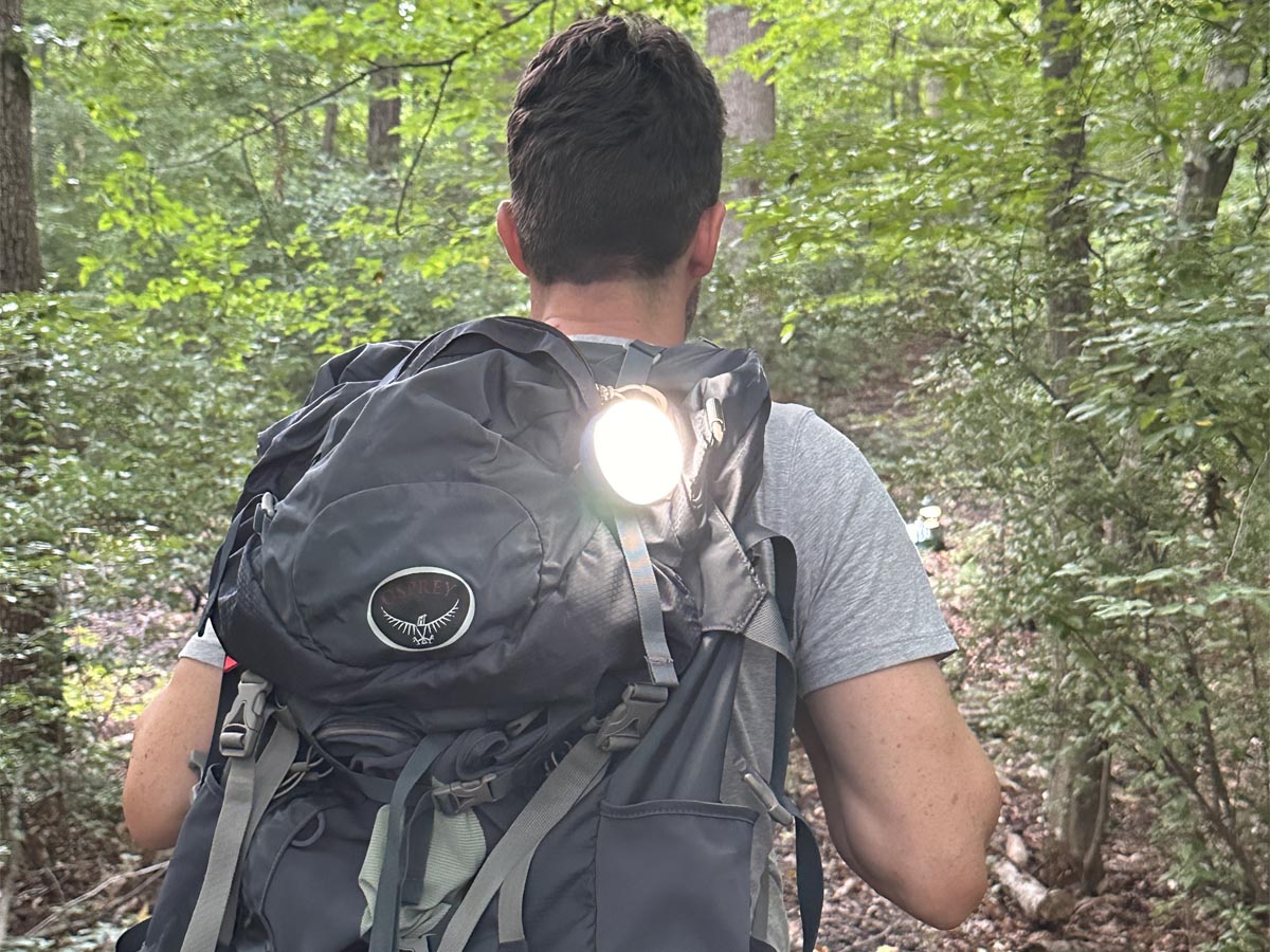 A person hiking in the woods with the best LED lantern option attached to their backpack to light the trail