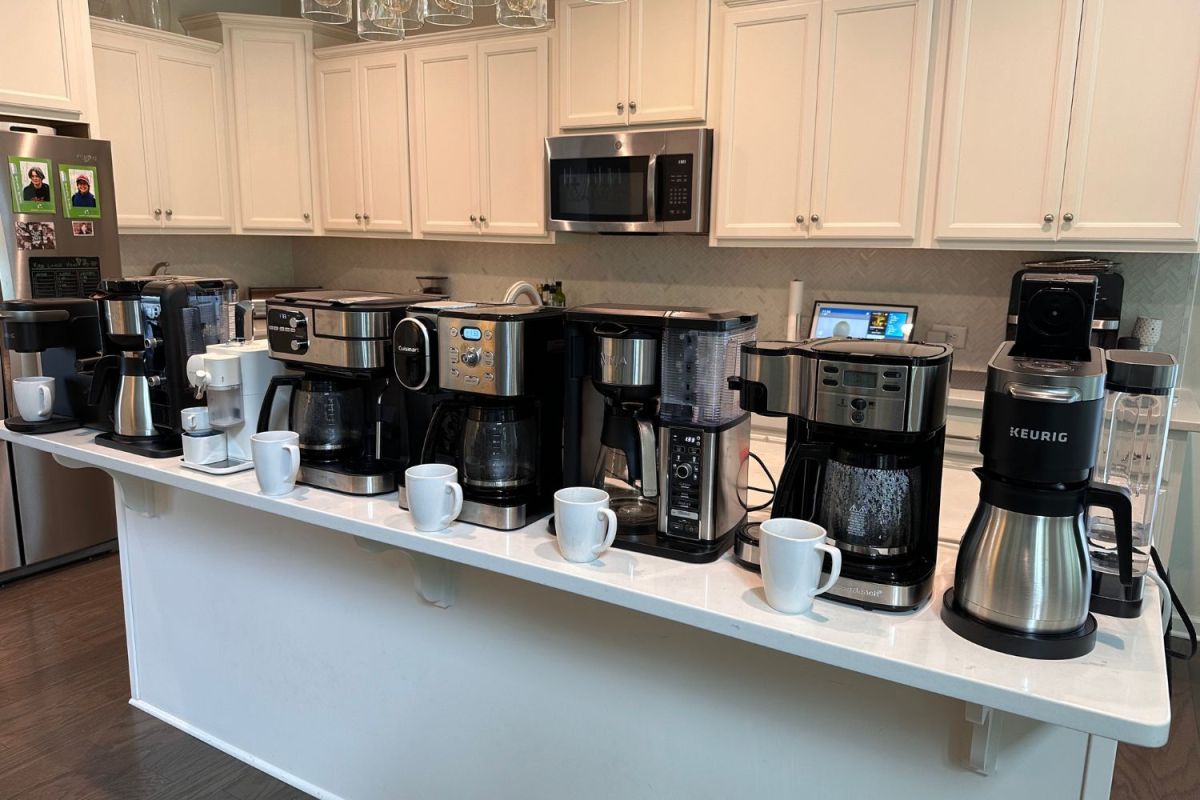A lineup on a kitchen island of the best dual coffee makers next to waiting coffee mugs
