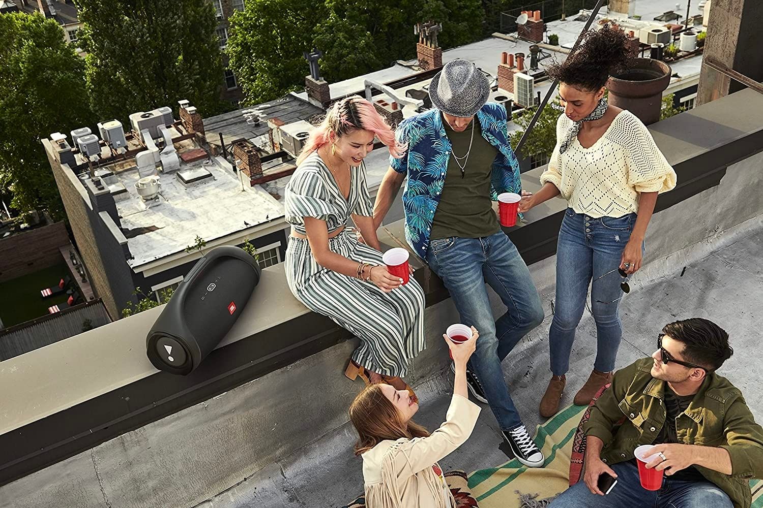 A group of friends on a roof enjoying drinks next to the best outdoor speaker