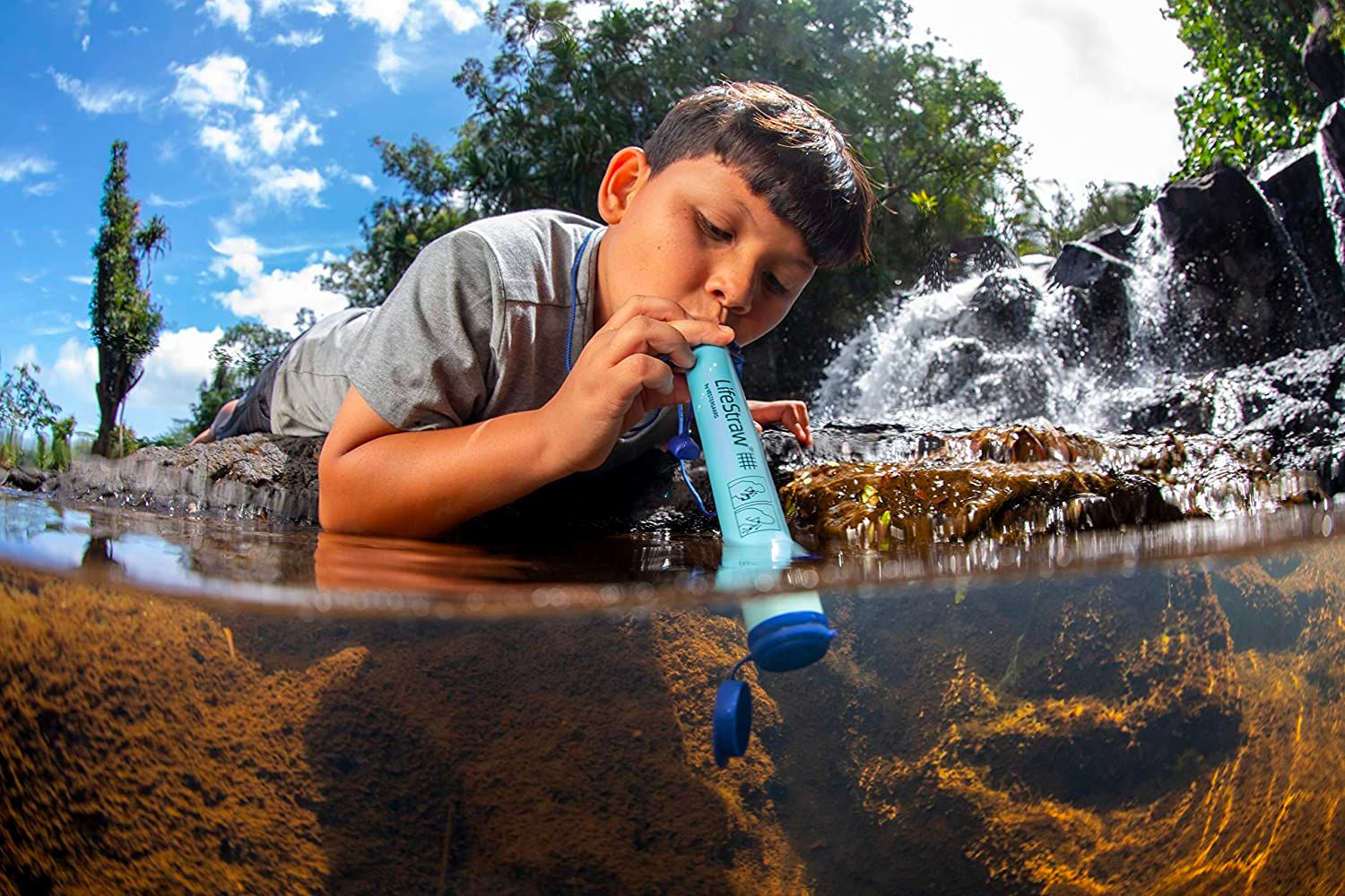 A young boy uses the best portable water filter option to get a drink from a stream