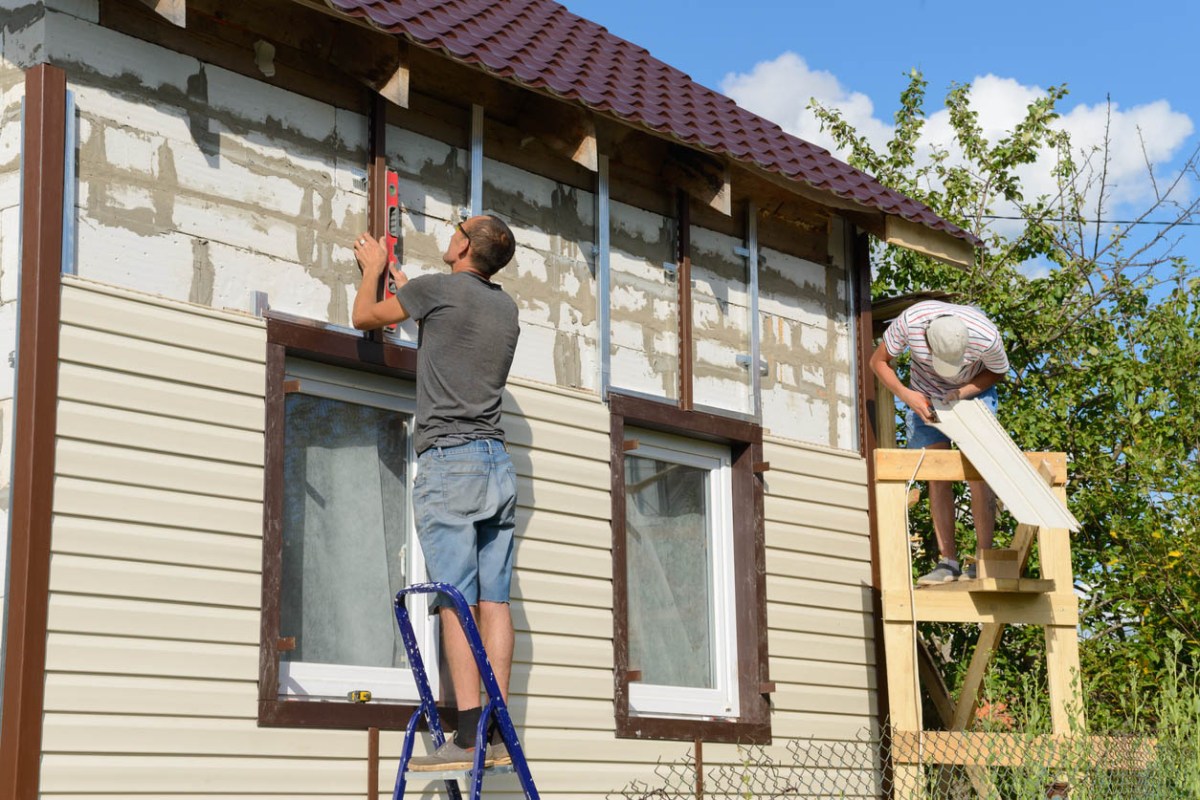 A view of a worker installing vinyl siding on a house.