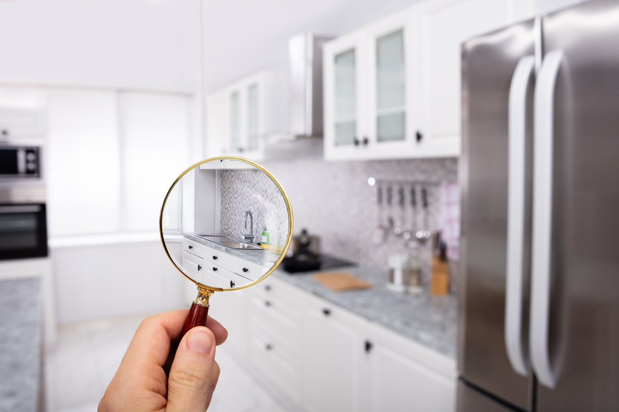 Close-up Of A Man's Hand Holding Magnifying Glass Over The Kitchen In Modular Kitchen