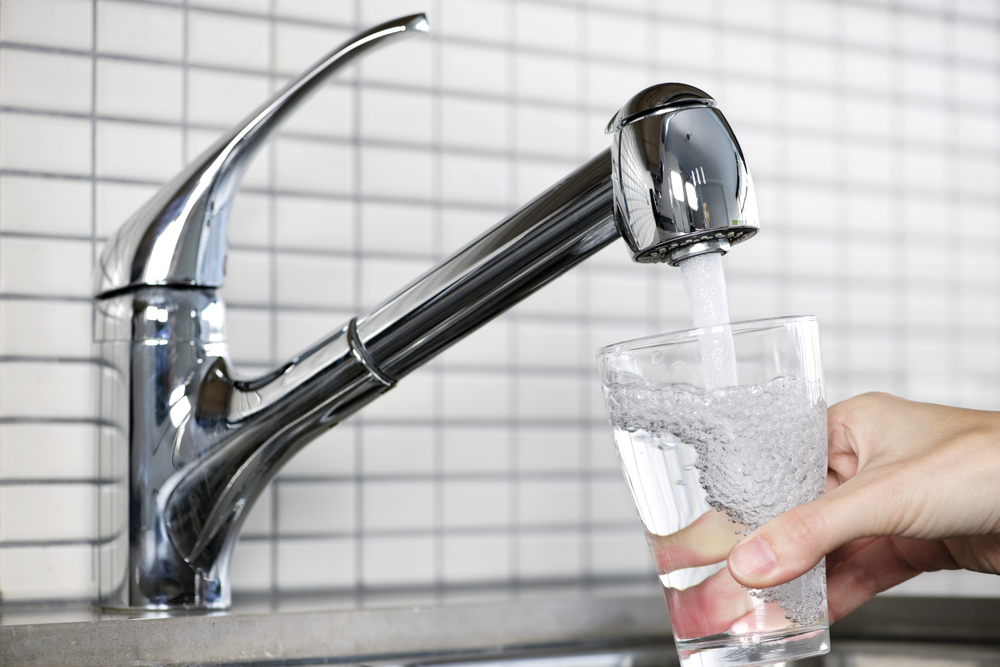 A person getting a glass of water from a kitchen faucet that's hooked up to the best whole house water filter option