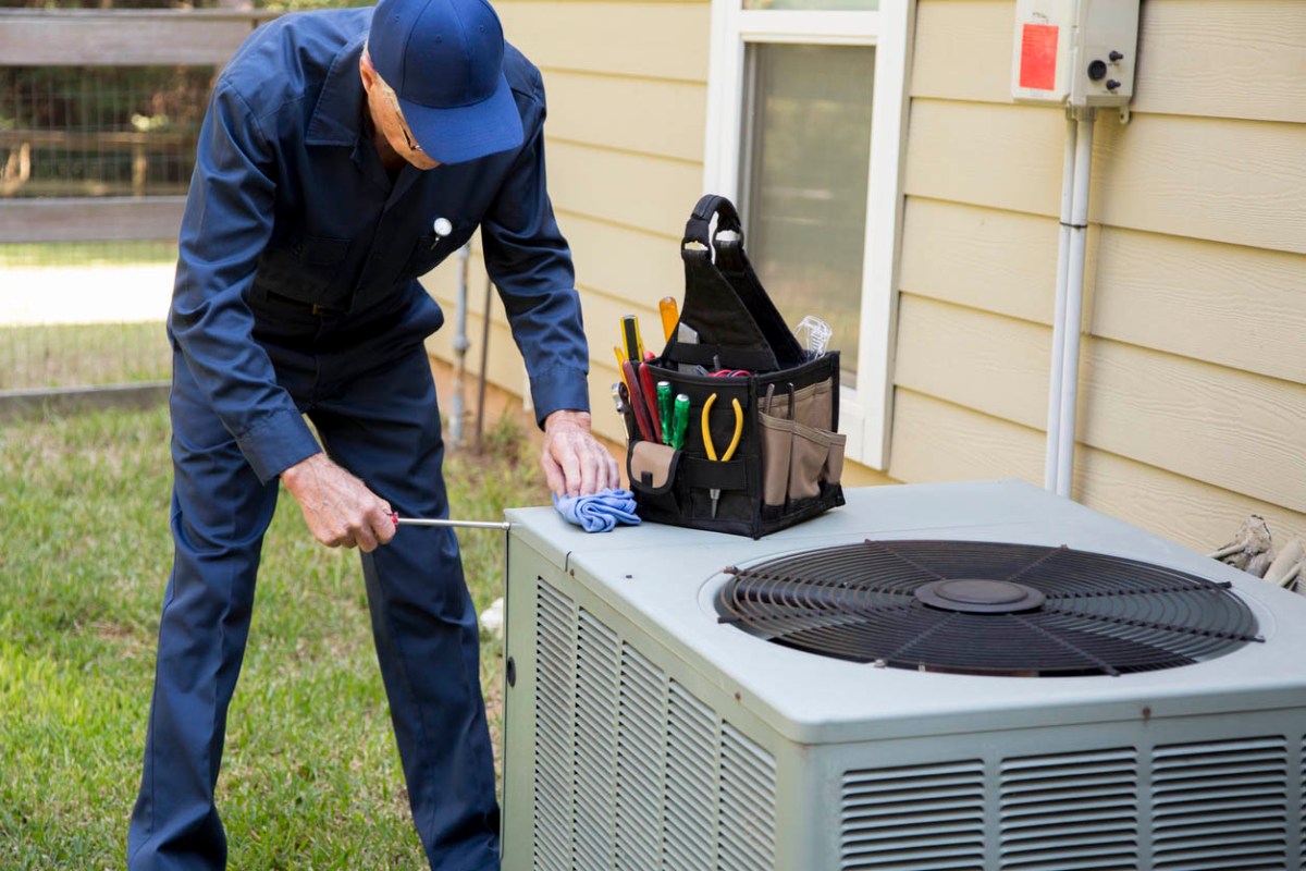 A worker in a blue suit installs an AC unit outside a home.
