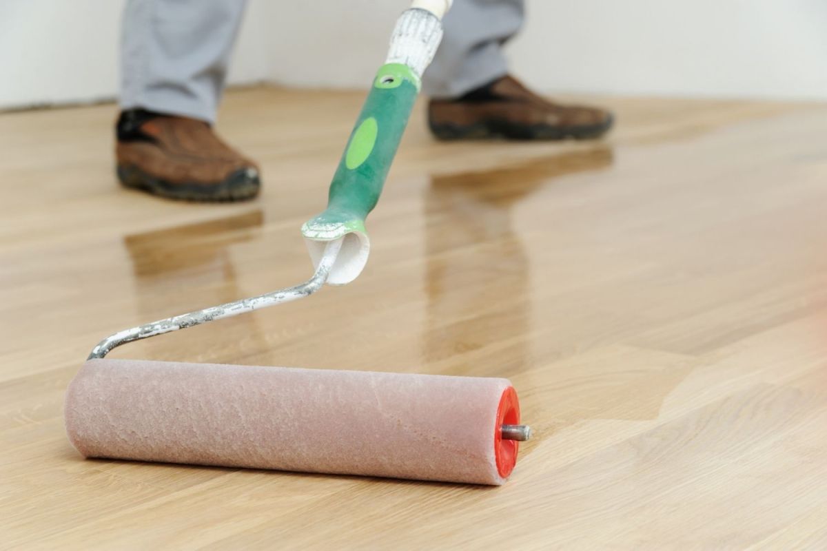 A person using a roller brush to apply the best water-based polyurethane for floors option