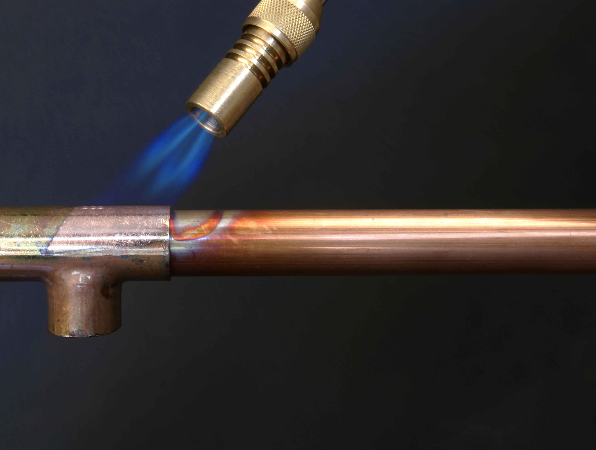 "Benzene torch heating a joint in copper piping, focus on pipe."