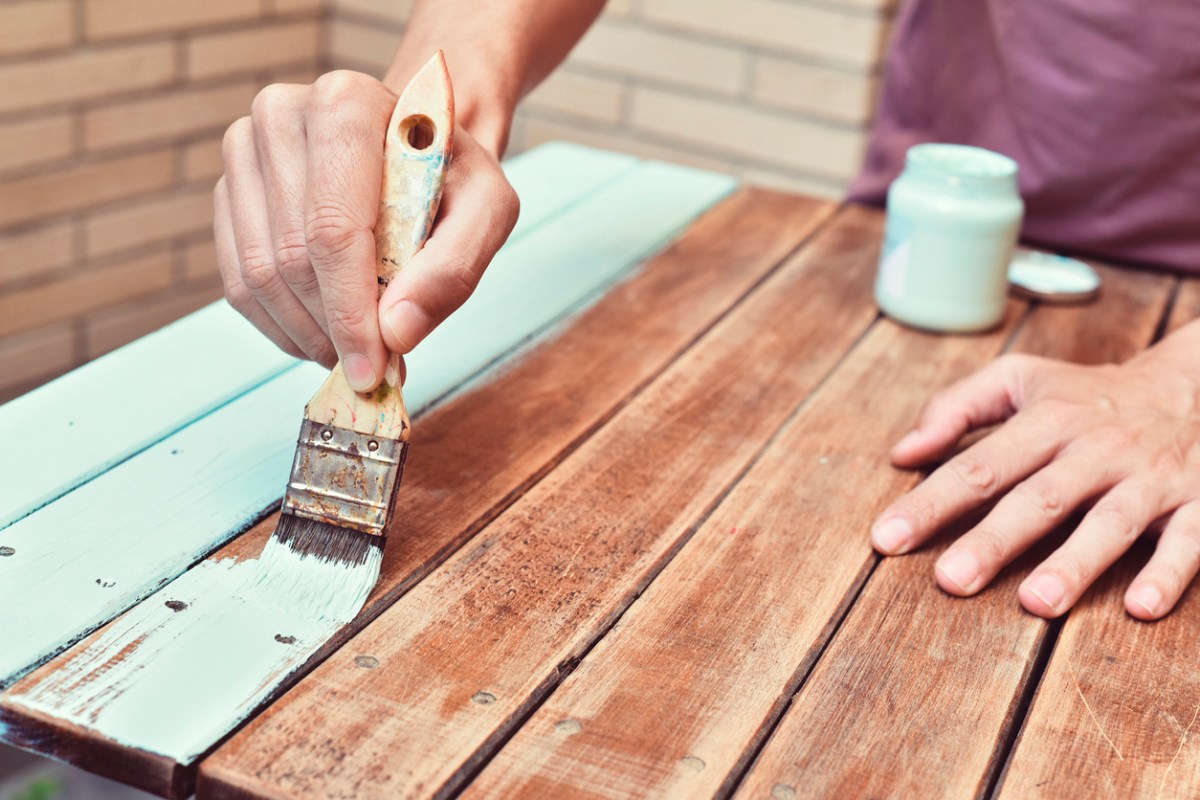 closeup of a young caucasian man painting an old wooden table with a brush