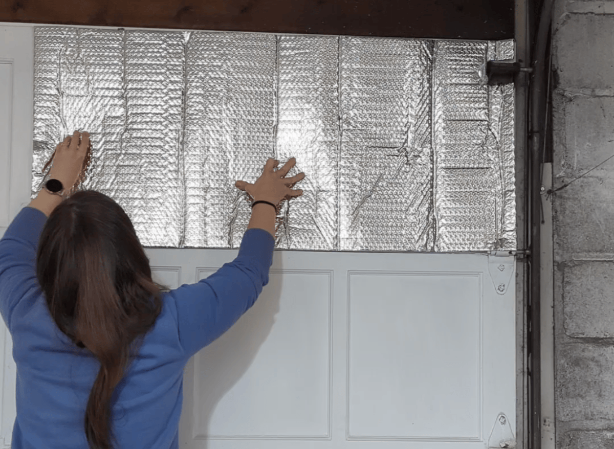 Back view of woman affixing insulating panels to a garage door.