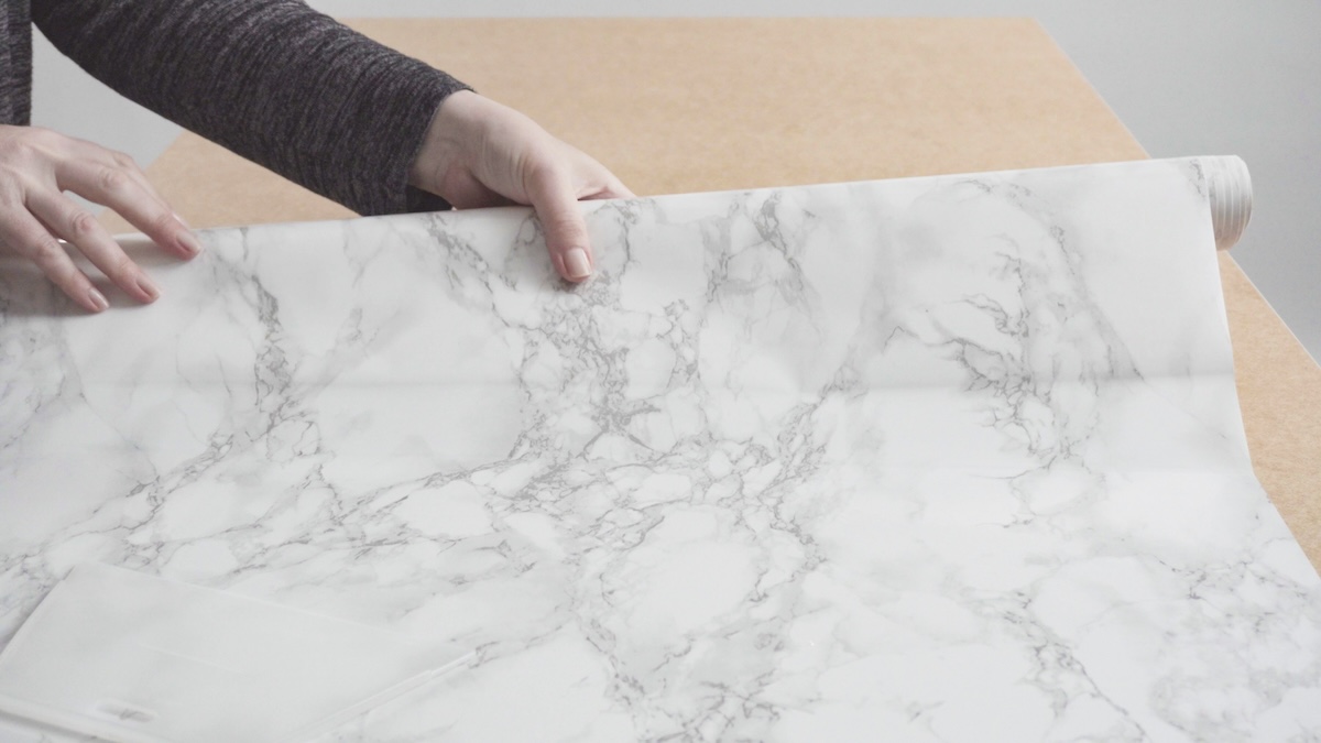 A woman lays marble contact paper onto a kitchen counter.