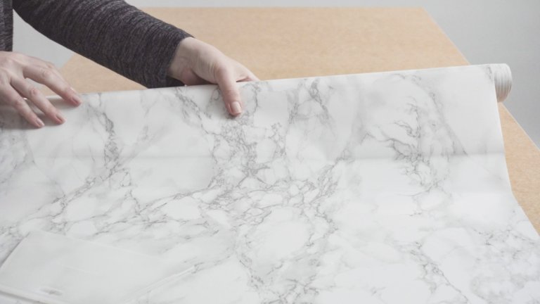 A woman lays marble contact paper onto a kitchen counter.
