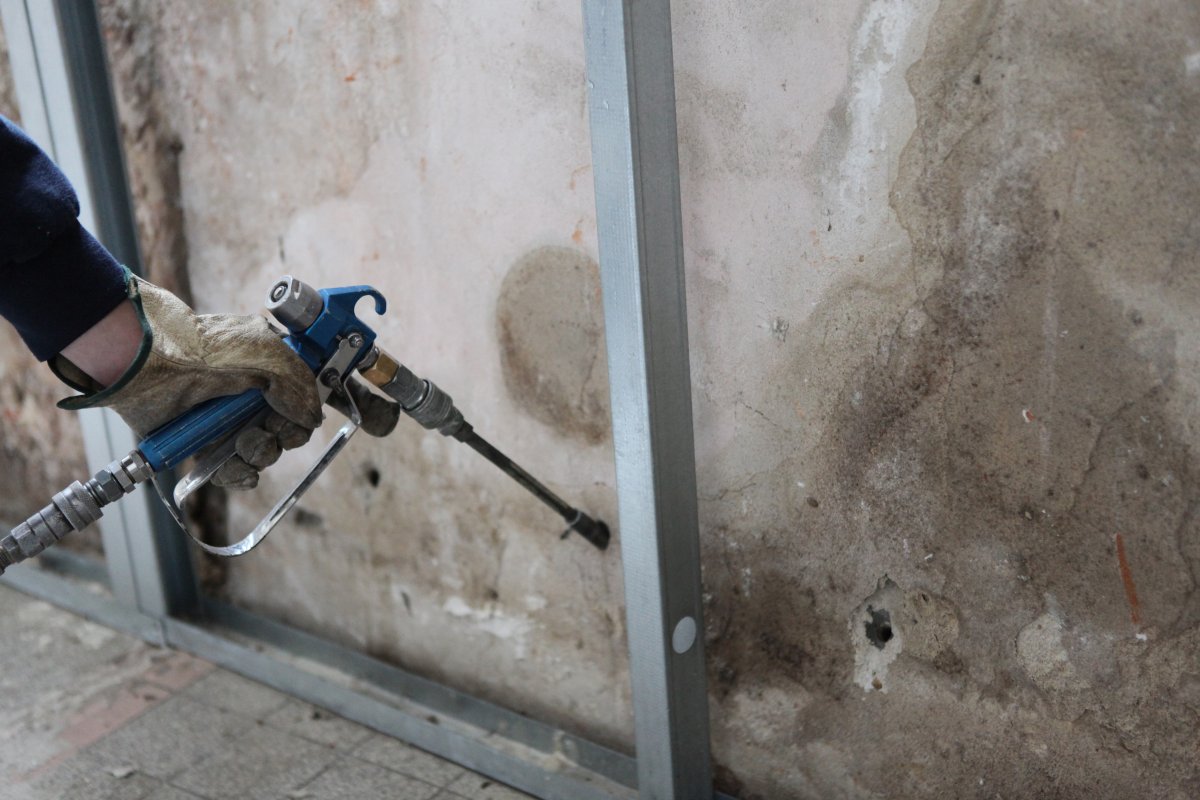 Close up view of person's hand spraying foam insulation into garage wall.