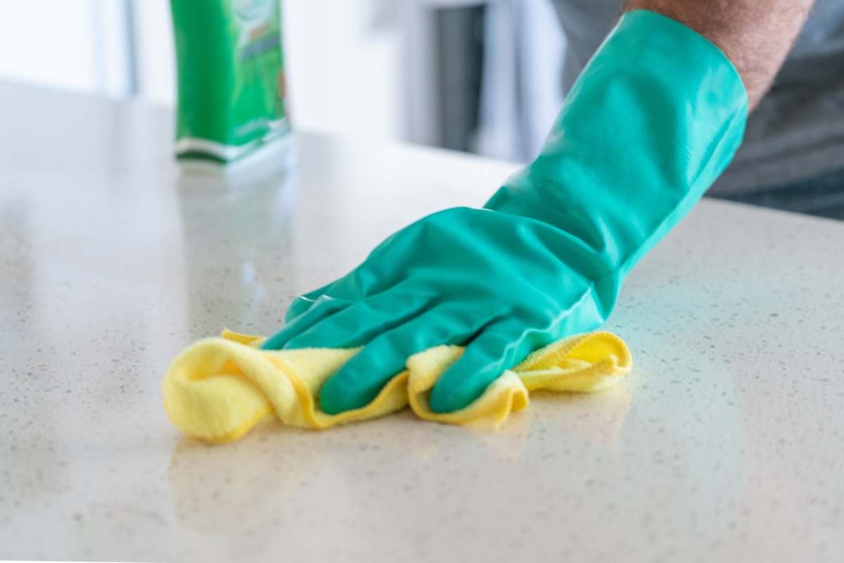 A hand wearing rubber glovers wipes a countertops with a rag.