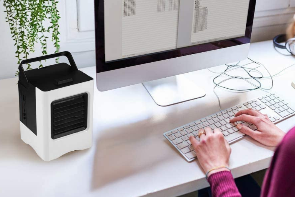 The best personal air conditioner option sits on a desk by a woman working on a computermay