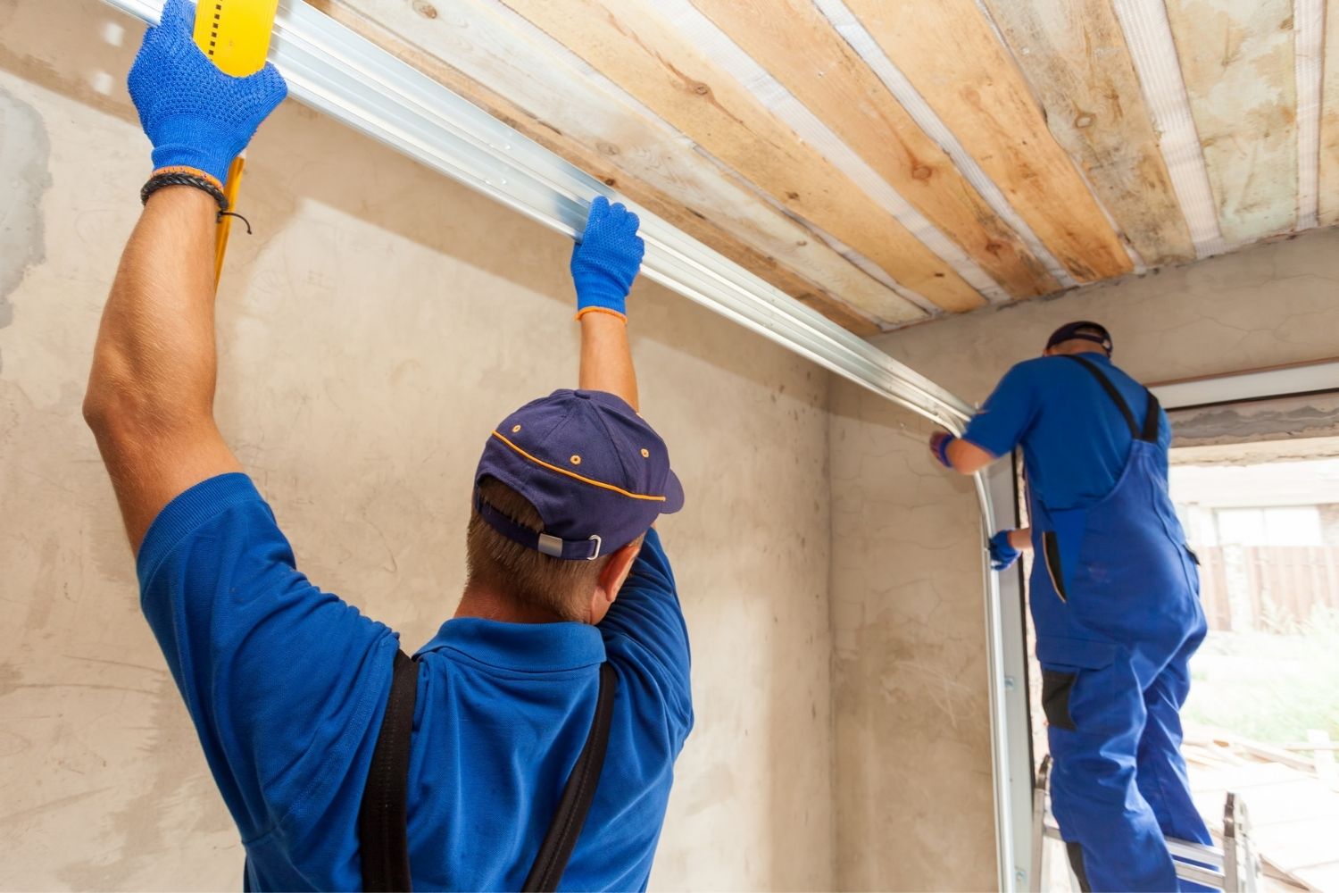 Two workers dressed in blue renovate a garage.