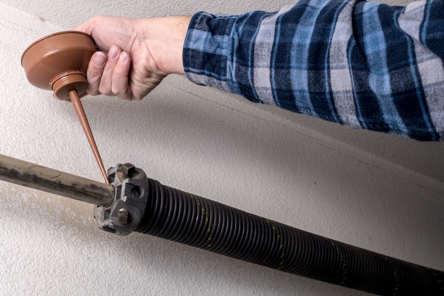 A close up of a garage door component and a person in a plaid shirt using a tool to fix it. 