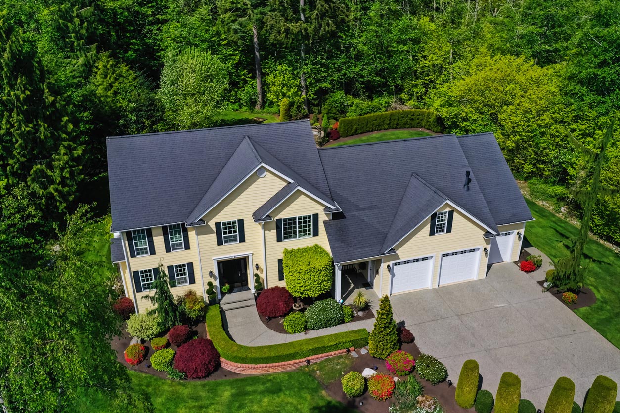 Aerial view of a two-story home with an attached garage, beautifully manicured landscaping, and mature trees.