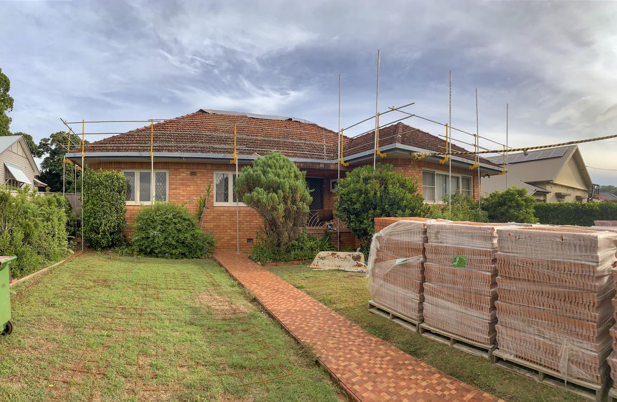 A one-story home with pallets of roof tile sitting in the backyard waiting to be installed.