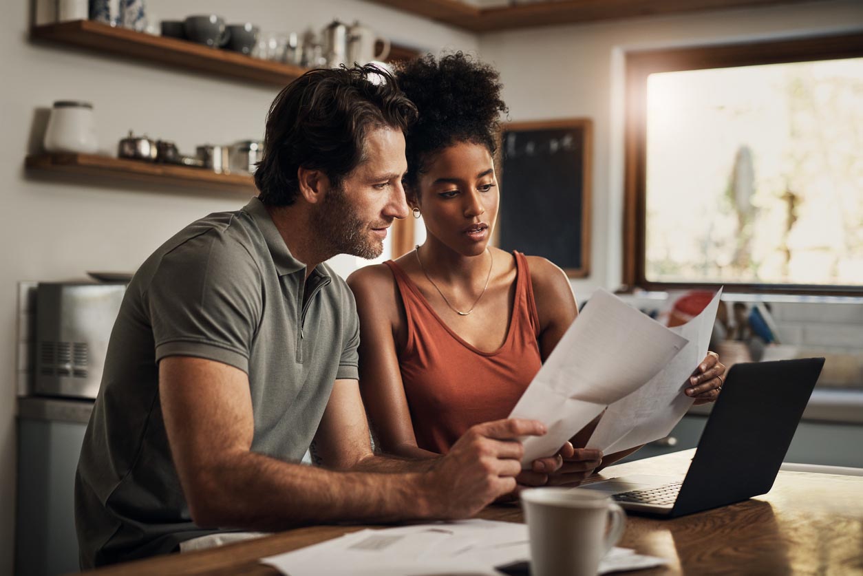 A man and a woman look over documents in front of a laptop.