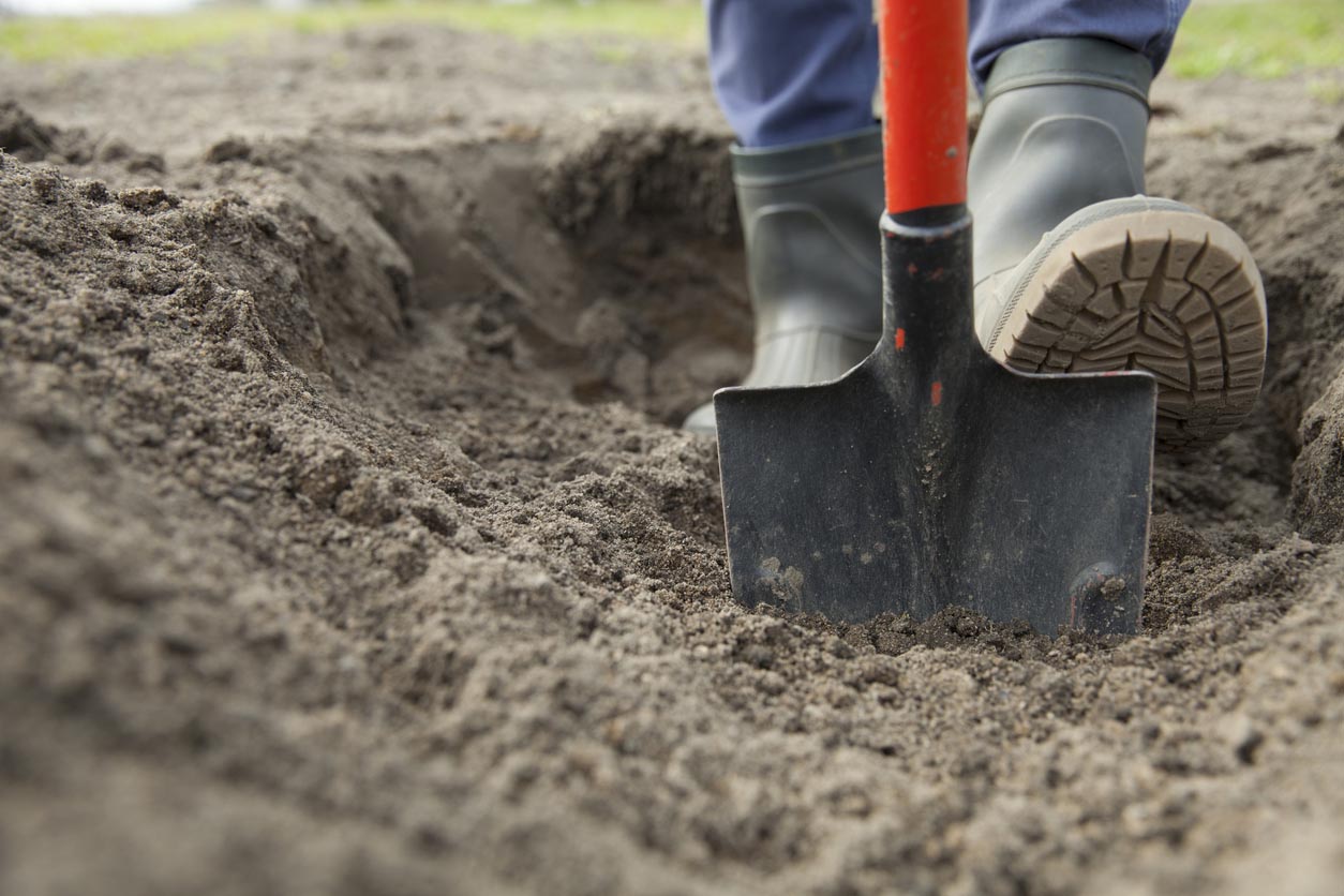 A close up of a person digging ground with a shovel.