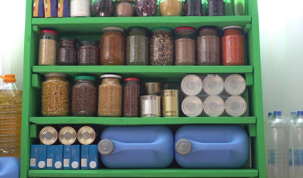 Green plastic shelving with jars and cans of food, and plastic water jugs. Emergency food and water storage.