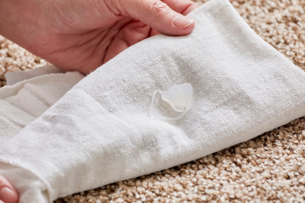 Woman uses white cloth to remove hot glue from a brown carpet.