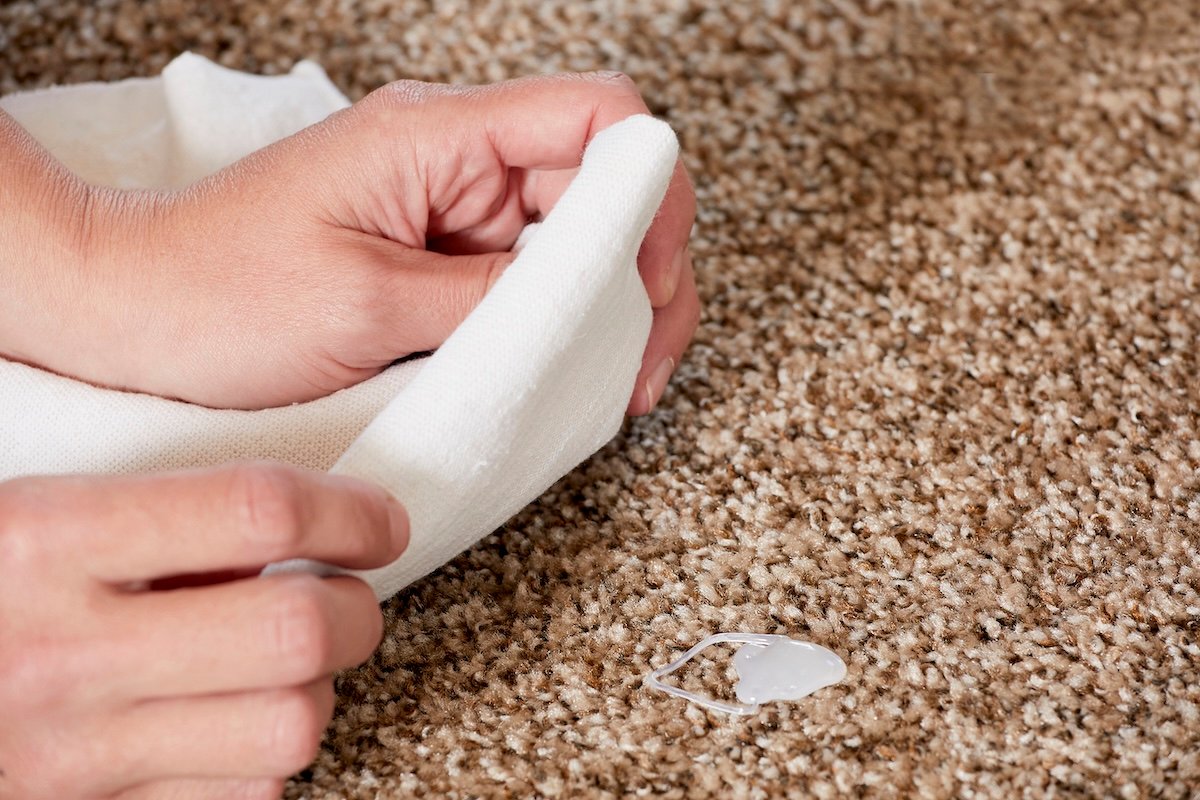 Woman places a folded white cloth over a spot of hot glue on a brown carpet.