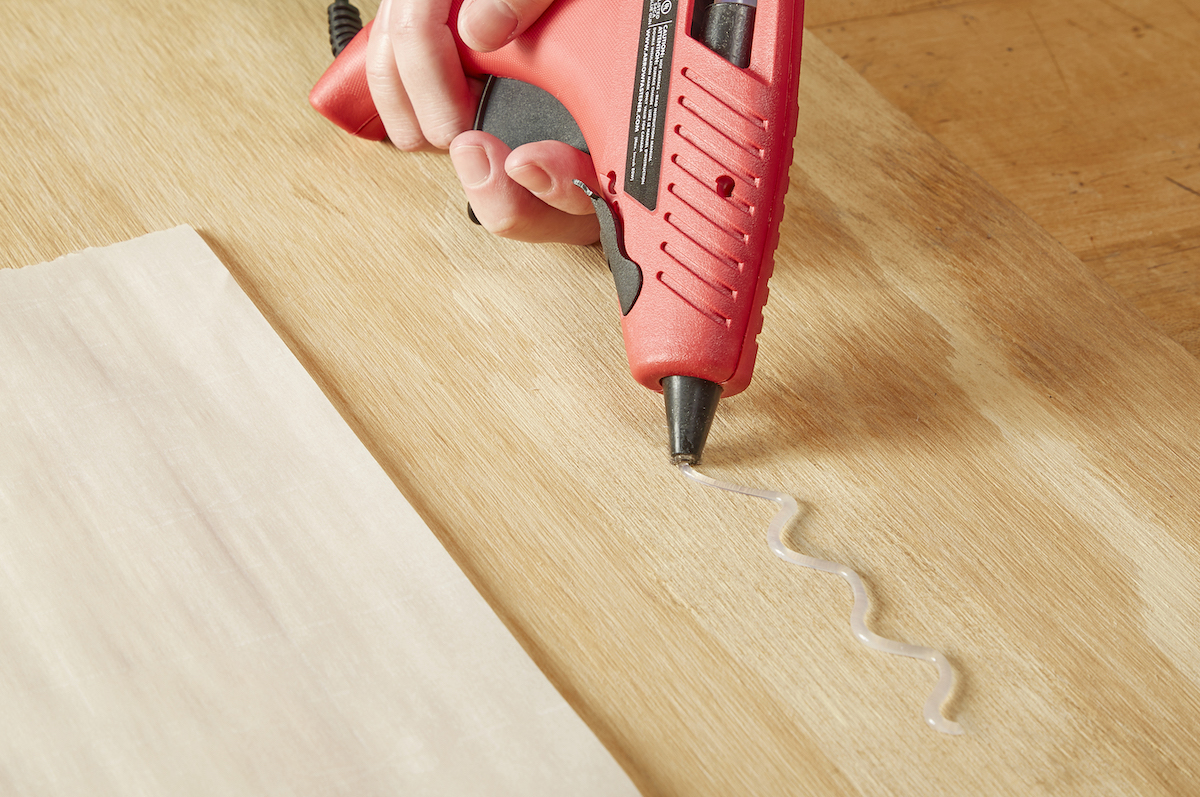 Woman extrudes hot glue onto a wooden surface from a red glue gun.
