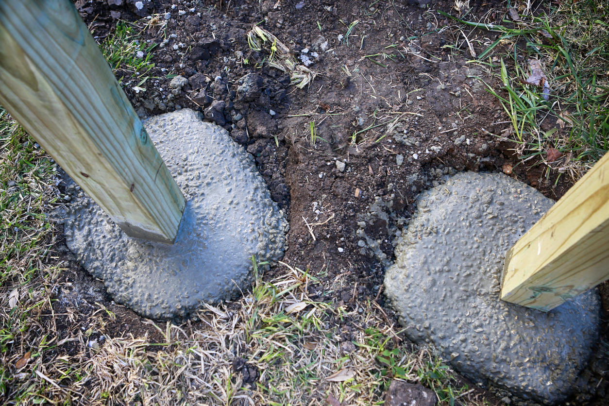 Building a fence in progress: setting up wooden poles in concrete foundation.