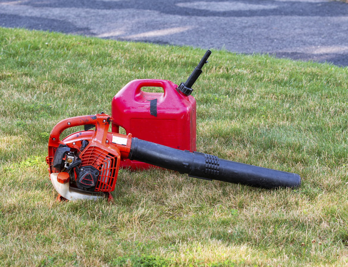 A landscapers leaf air blower with a gas can lying on the ground of a residential green grass lawn.