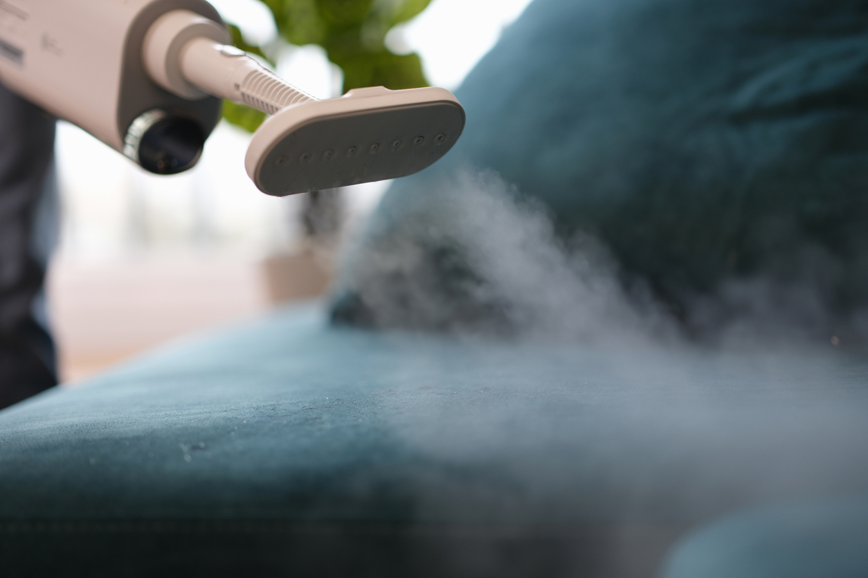 A vacuum cleaner cleans dirty upholstered furniture with steam, close-up.