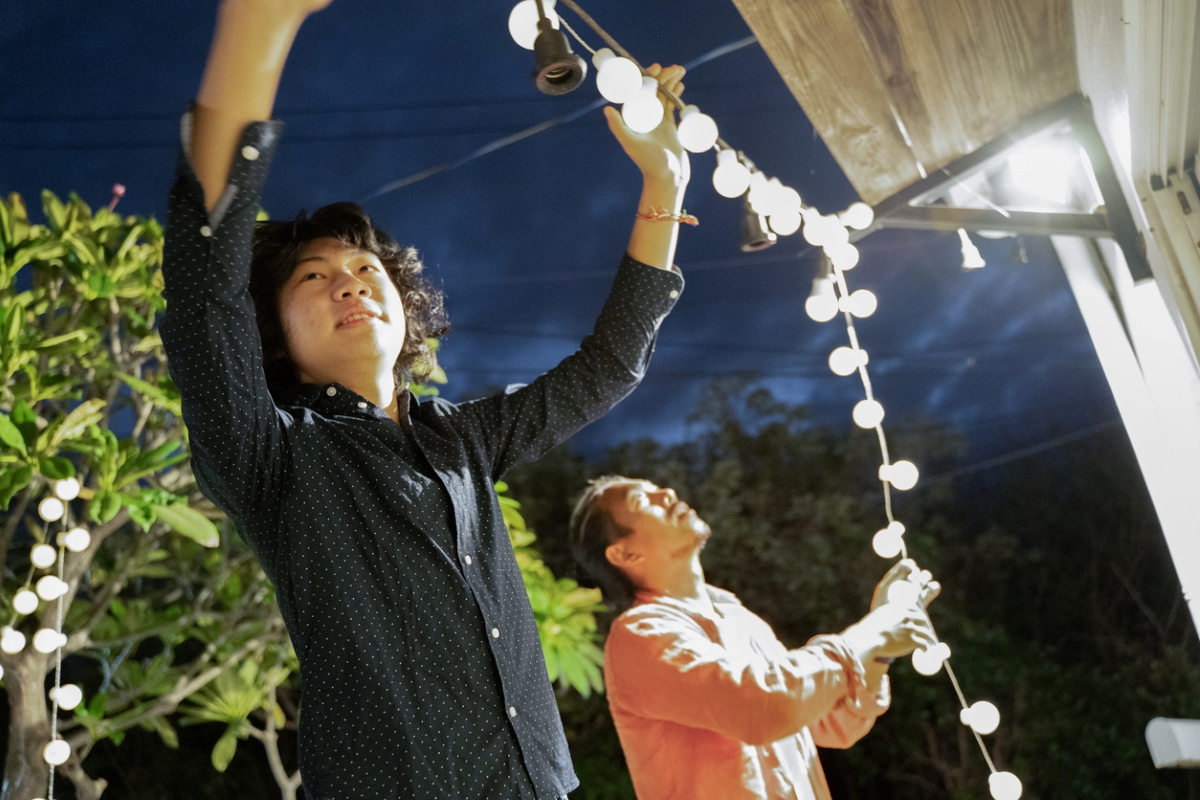 Two Asian men working together to string lights outside home