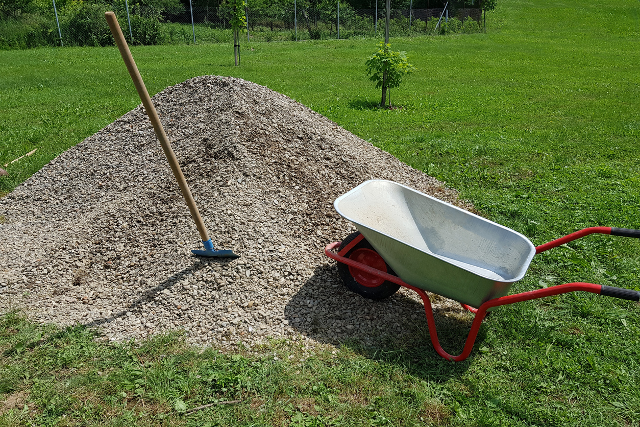 Construction wheelbarrow shovel on a pile of a rock gravel in a garden.