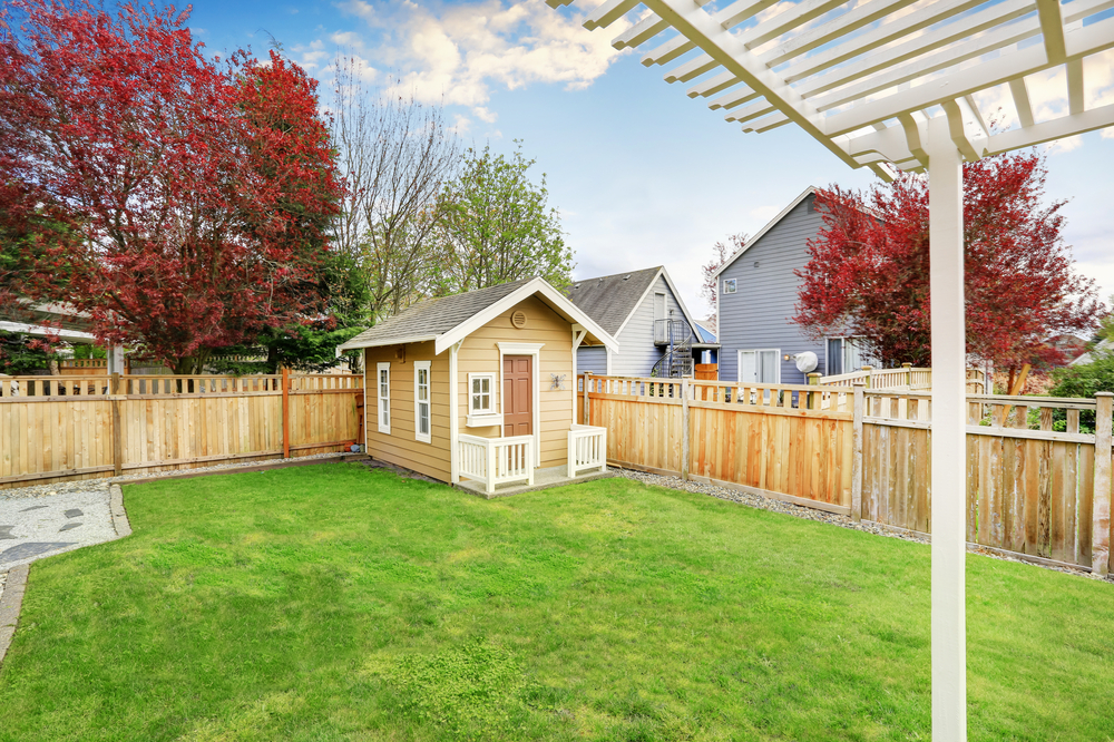 A fully built shed located in a grassy yard with a wood fence behind it.