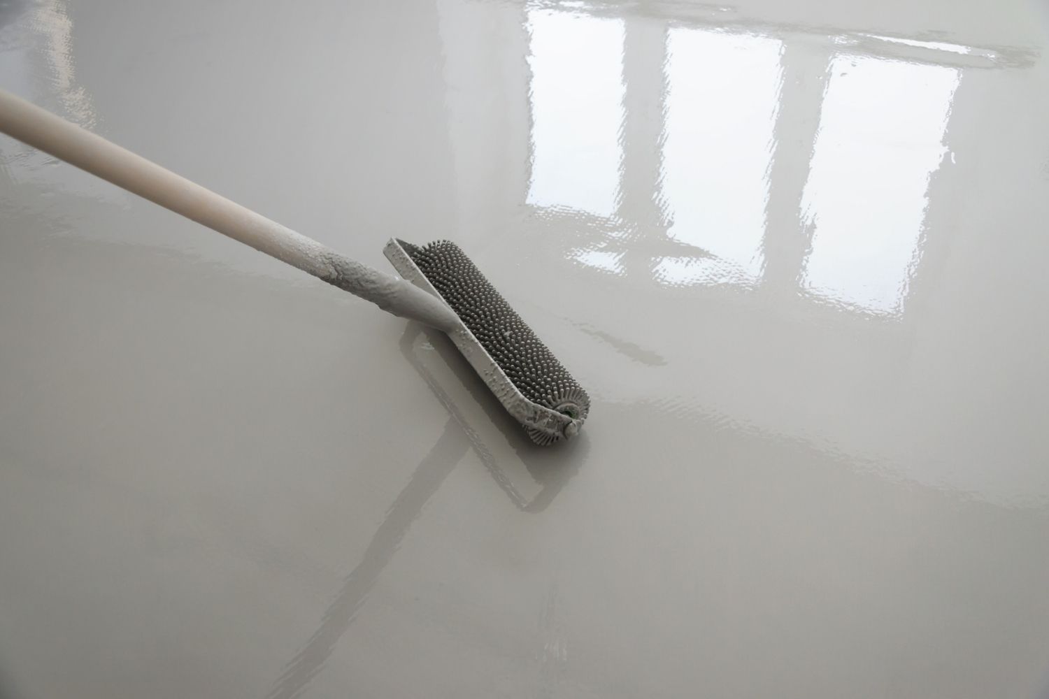 A roller in the middle of applying epoxy coating to a garage floor.