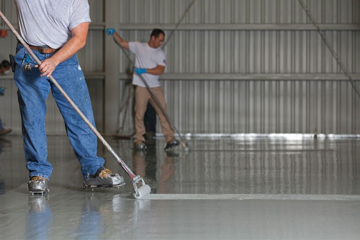 Two workers apply epoxy coating to a garage floor.