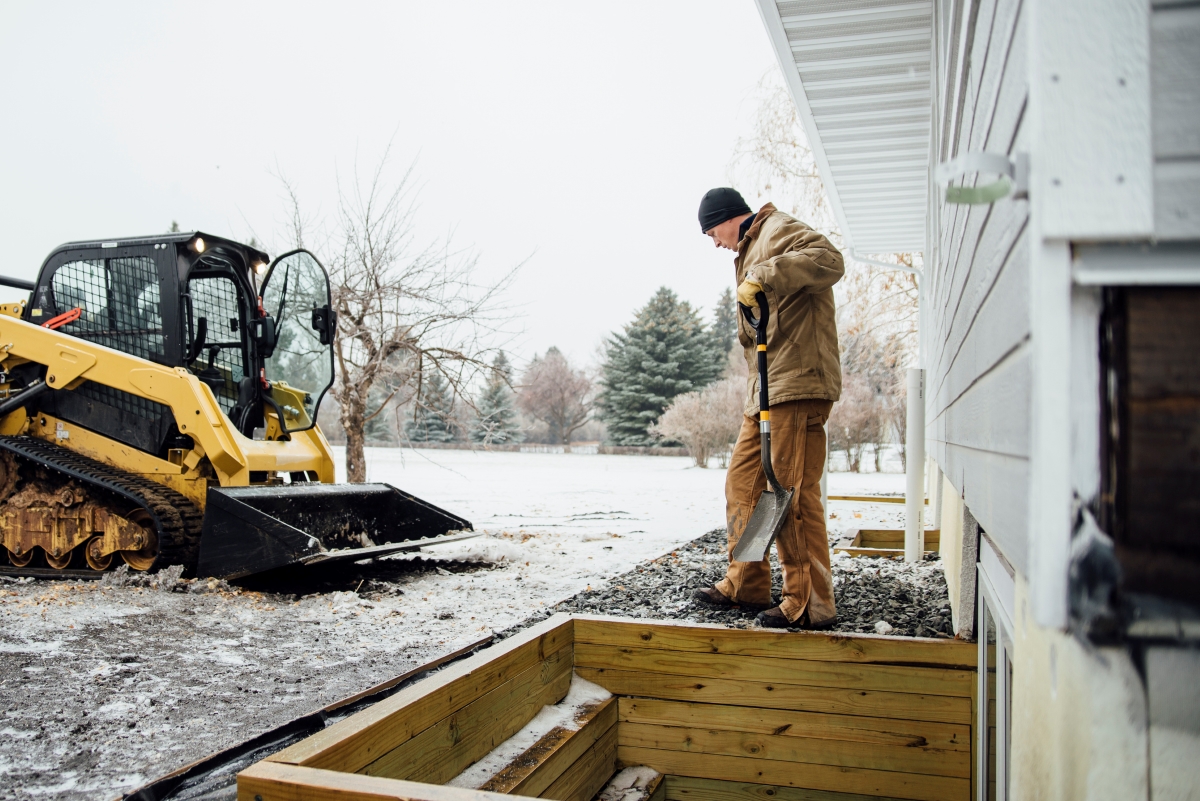 A man working on a wooden retainer wall in winter.