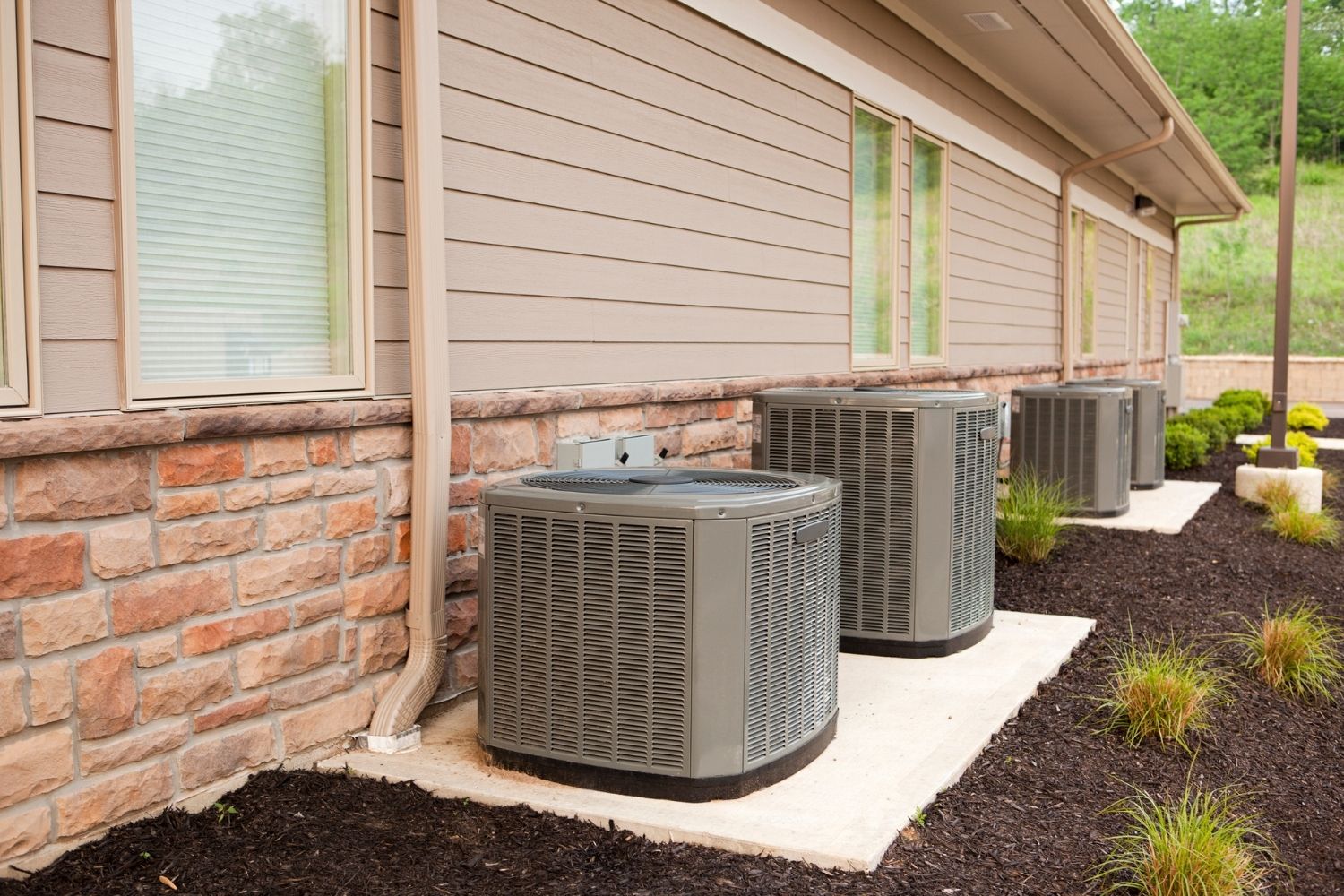 A row of HVAC units lined up against a house.
