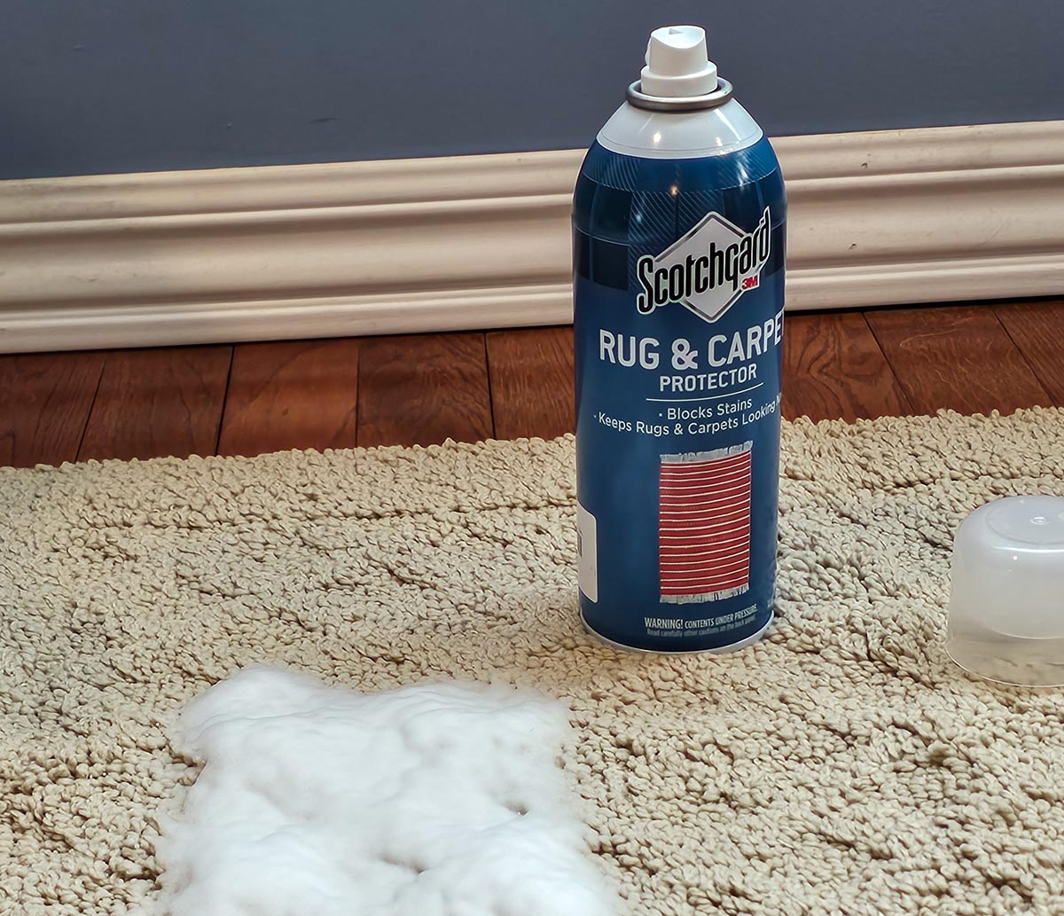 A can of Scotchgard Rug & Carpet Protector next to a pile of foam on beige carpet.