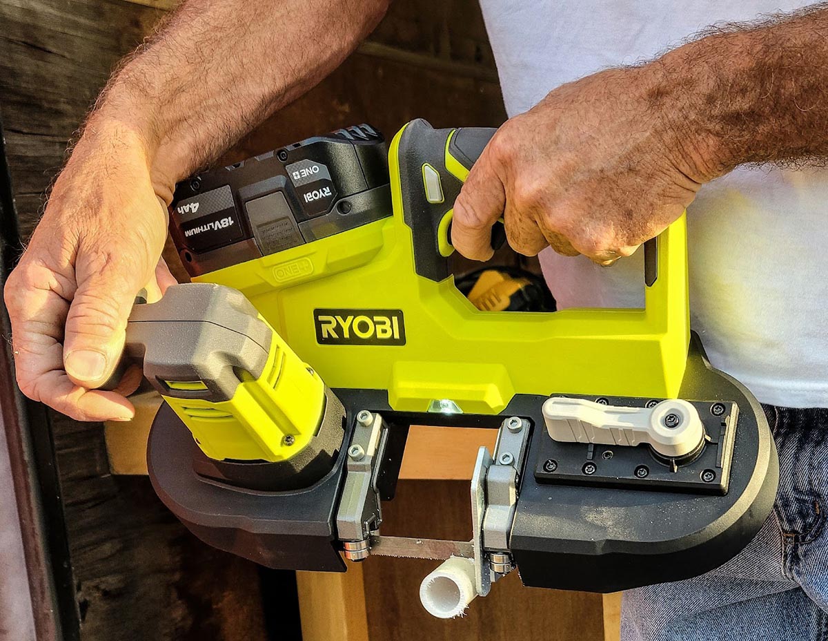 A person using the Ryobi P590K1 One+ 18V Cordless Band Saw Kit to cut a piece of PVC pipe during testing.